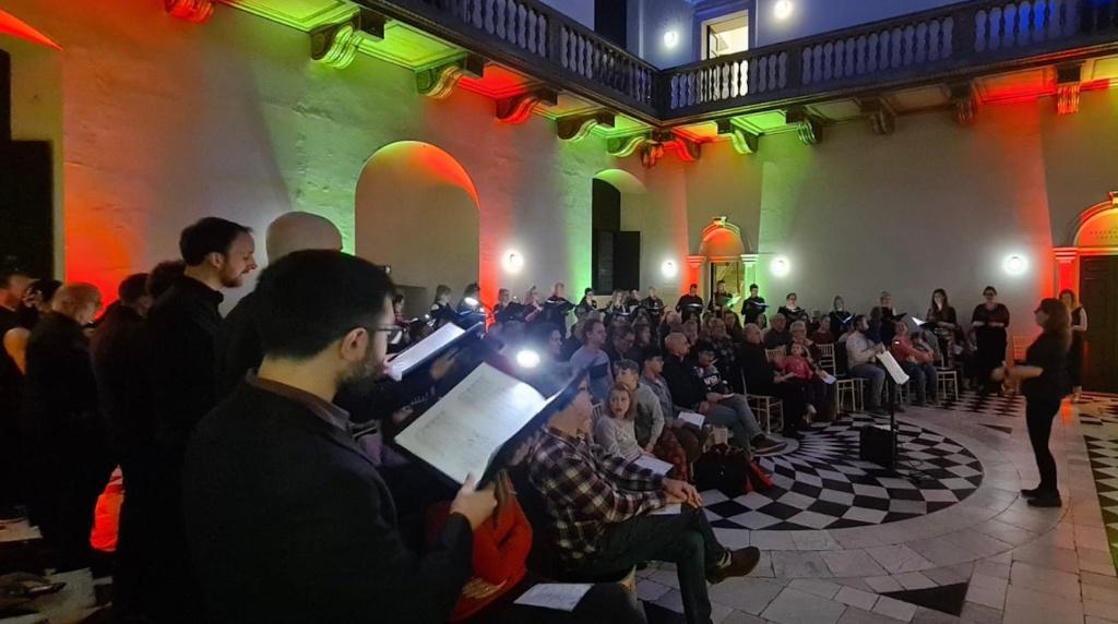 A choir sing in the Great Hall of the Queen's House lit in green and red lighting
